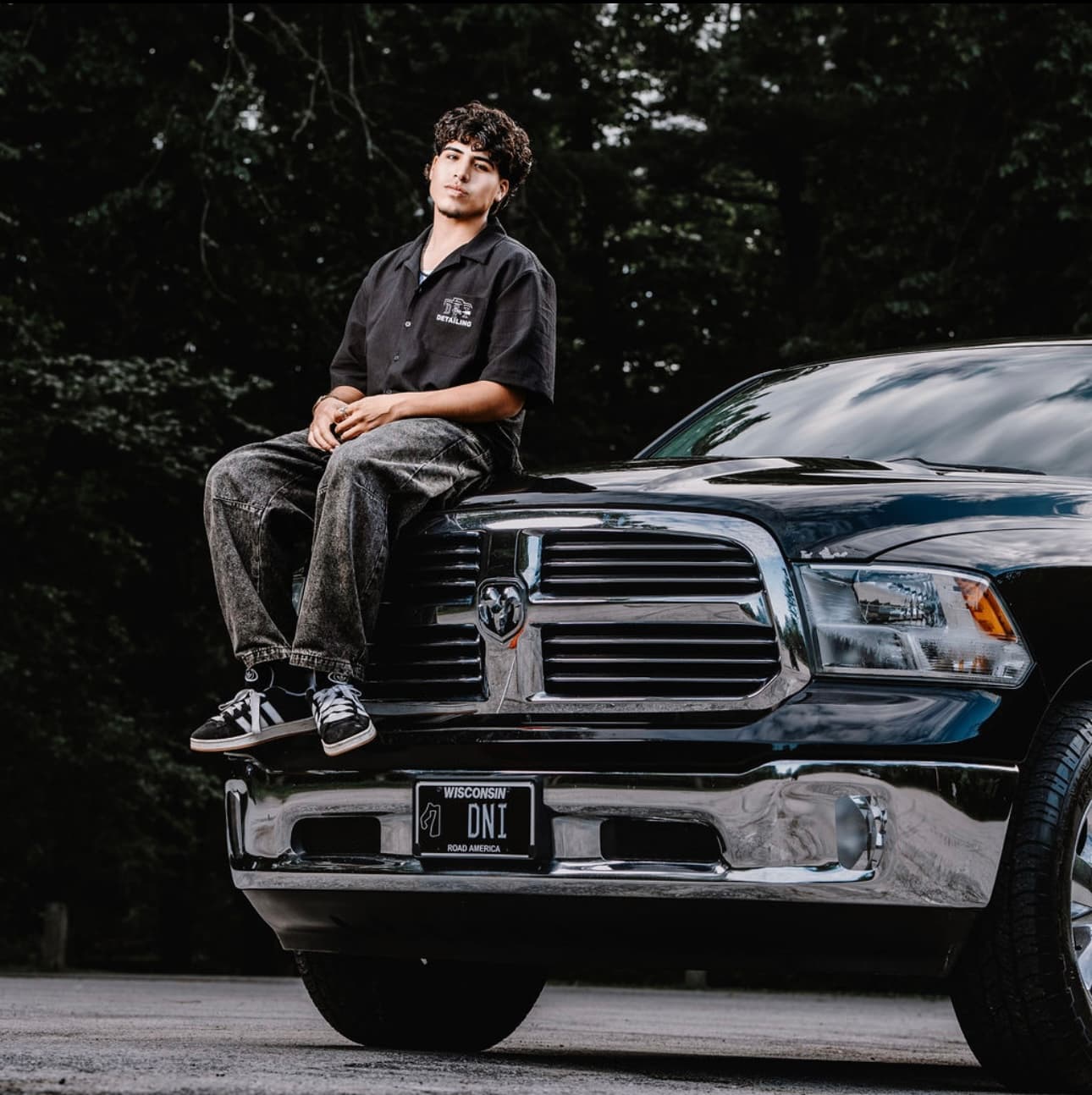Isaiah sitting on the hood of his black Ram truck with the Wisconsin DNI plate